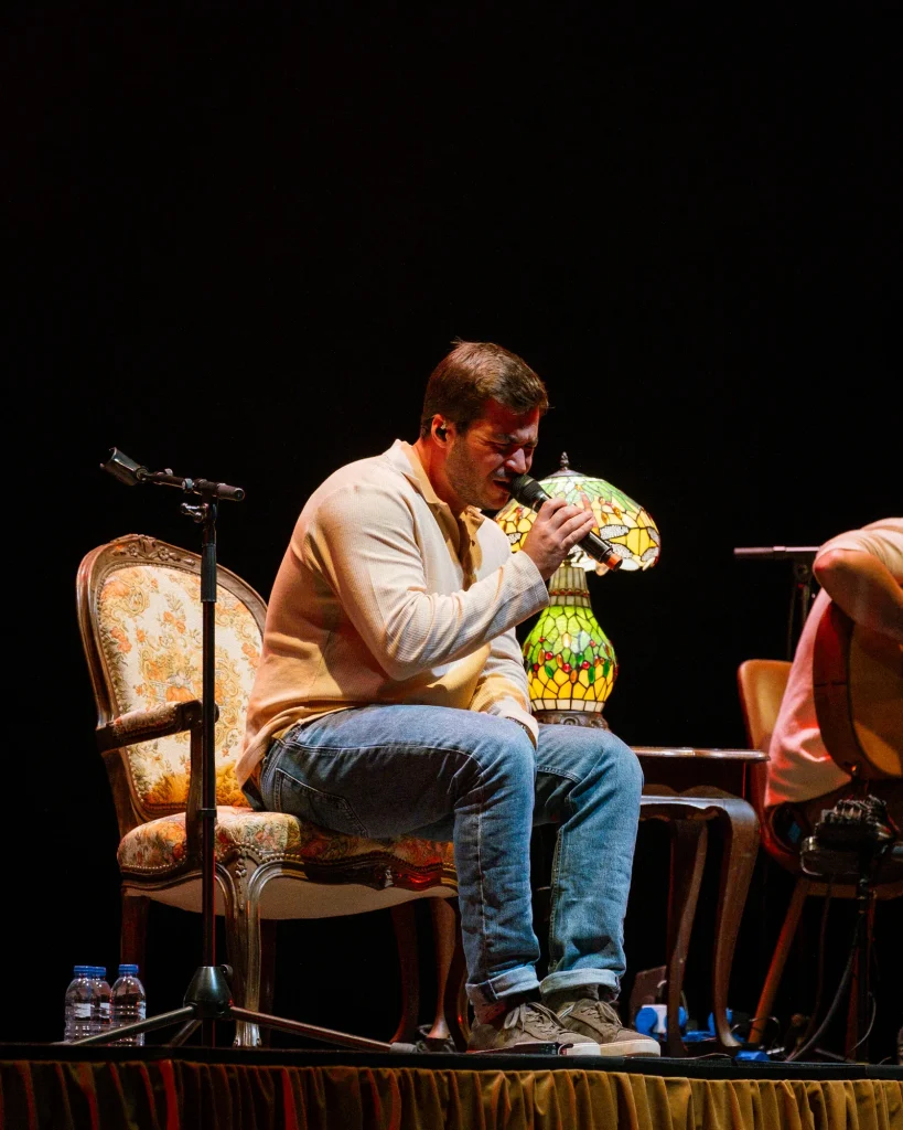 Luís Trigacheiro sentado numa cadeira clássica, debruçado a cantar ao microfone, durante concerto no Quartel das Artes em 2025 — xpectrum fotografia de concertos.