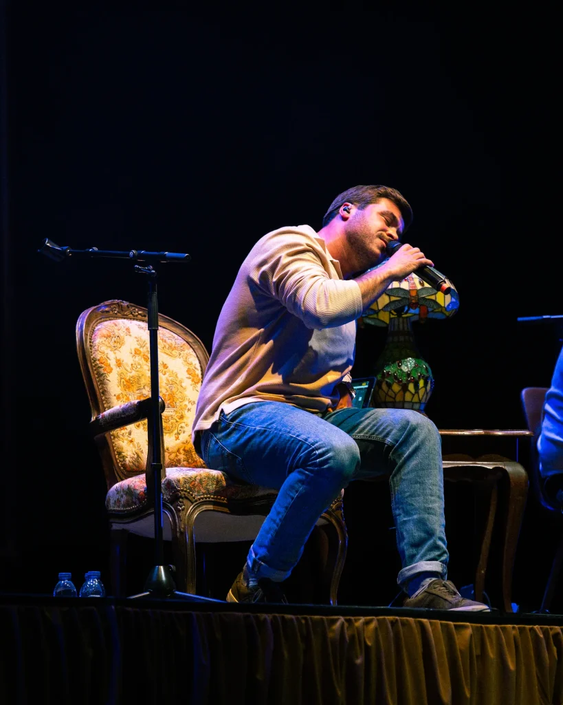 Luís Trigacheiro sentado no palco a cantar, em concerto no Quartel das Artes em 2025 — fotografia por xpectrum.