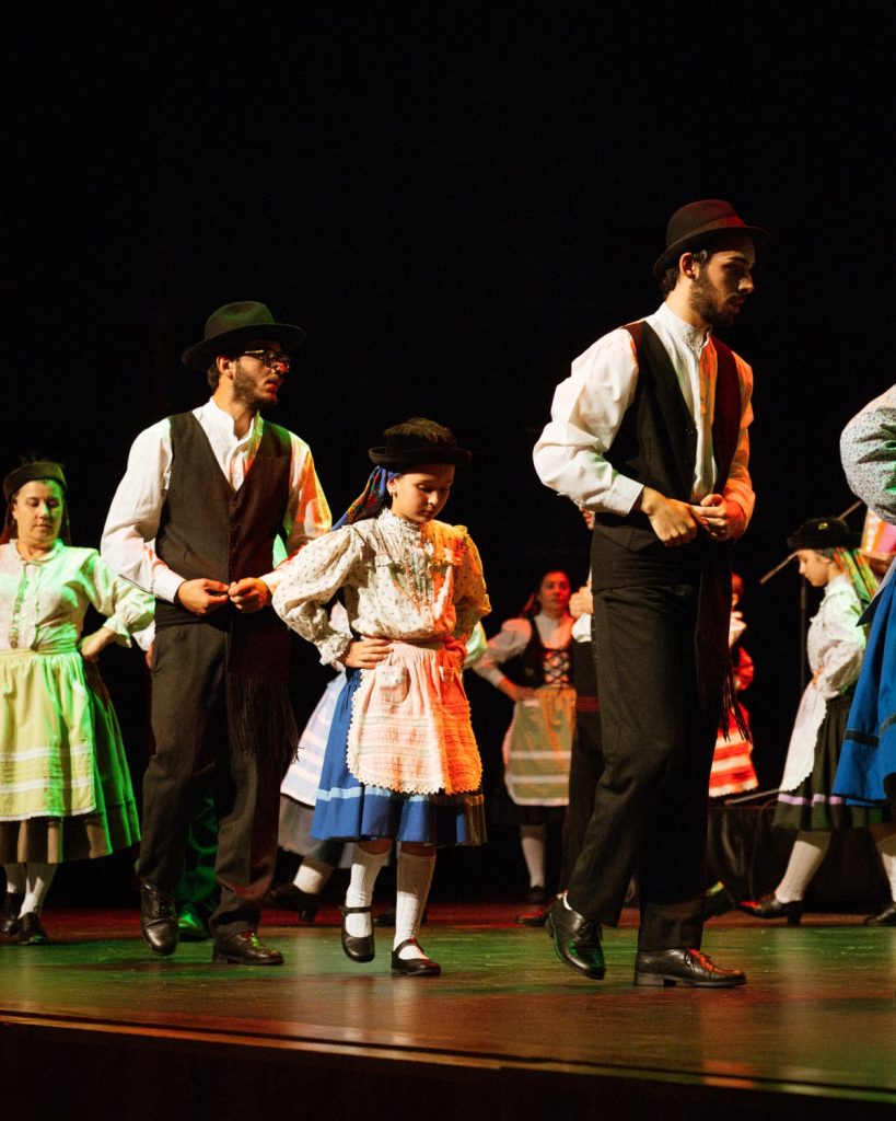 Dançarinos de rancho folclórico em trajes tradicionais portugueses no palco do Quartel das Artes durante o evento MOB 2025, incluindo uma criança a dançar