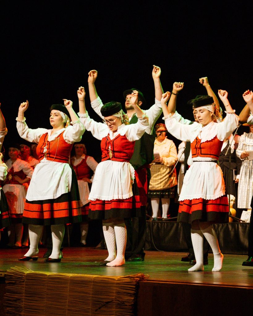 Grupo de bailarinas de rancho folclórico em trajes vermelhos, brancos e pretos com os braços levantados em coreografia no evento MOB 2025 no Quartel das Artes