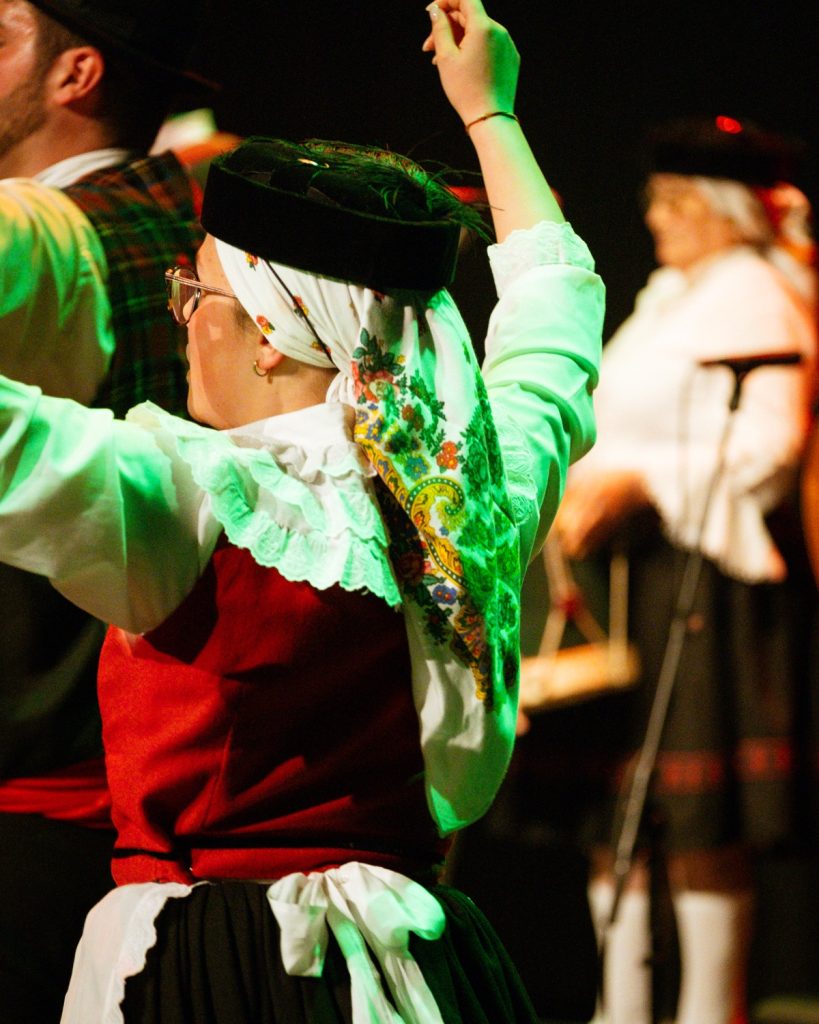 Retrato em close-up de bailarina de rancho folclórico com lenço floral colorido e traje vermelho, branco e preto no evento MOB 2025 no Quartel das Artes