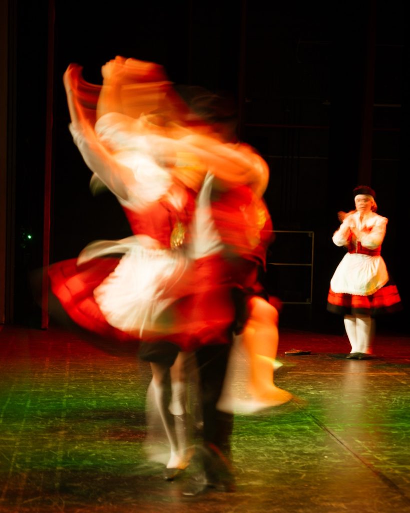 Bailarina de rancho folclórico em rotação captada com longa exposição, com saia laranja e vermelha em movimento no evento MOB 2025 no Quartel das Artes