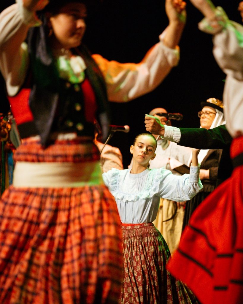 Jovem bailarina de rancho folclórico em traje tradicional com saia xadrez durante atuação no evento MOB 2025 no Quartel das Artes