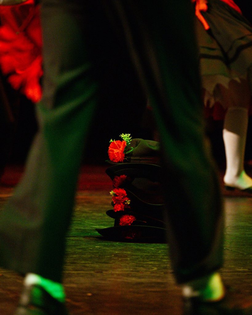 Chapéus tradicionais de rancho folclórico com flores vermelhas pousados no palco durante o evento MOB 2025 no Quartel das Artes