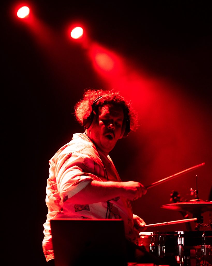 Sangue Suor no Quartel das Artes 2025 – baterista em close-up com expressão intensa em luz vermelha – fotografia de concertos xpectrum