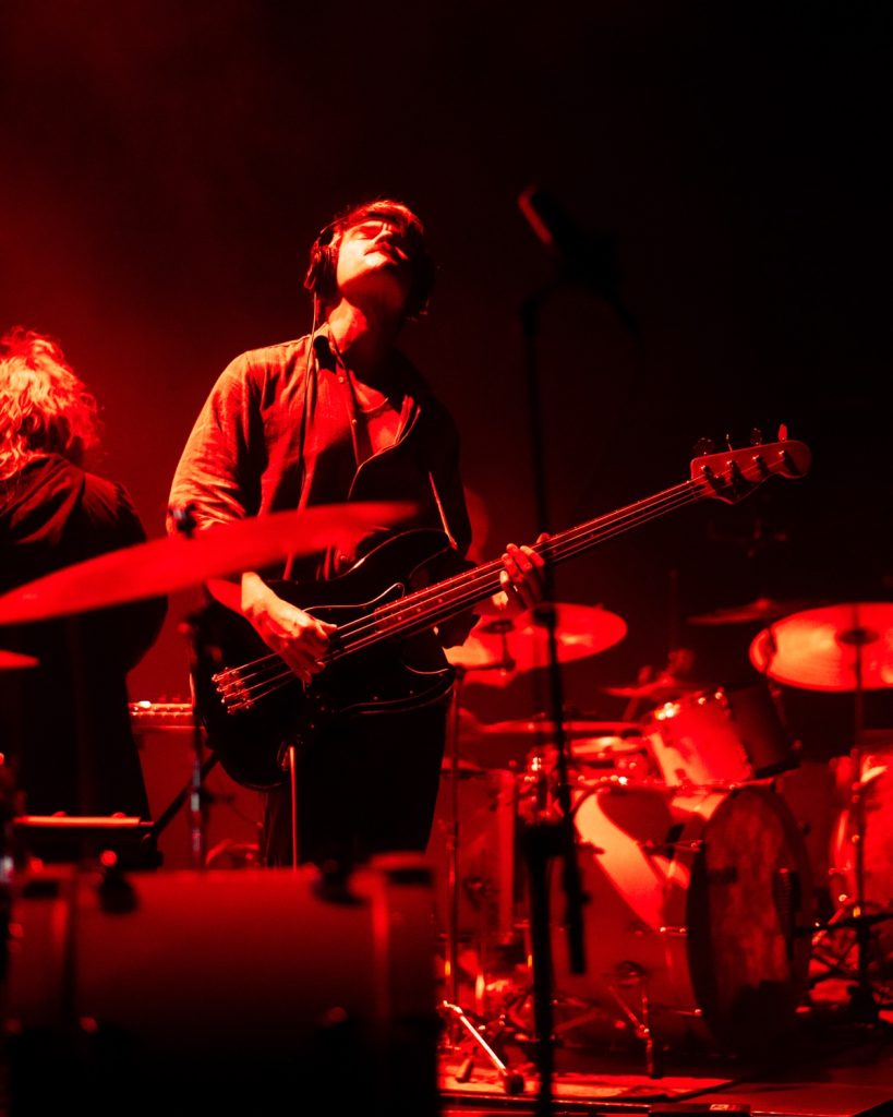 Sangue Suor ao vivo no Quartel das Artes 2025 – guitarrista com baixo a olhar para cima em luz vermelha – fotografia de concertos xpectrum