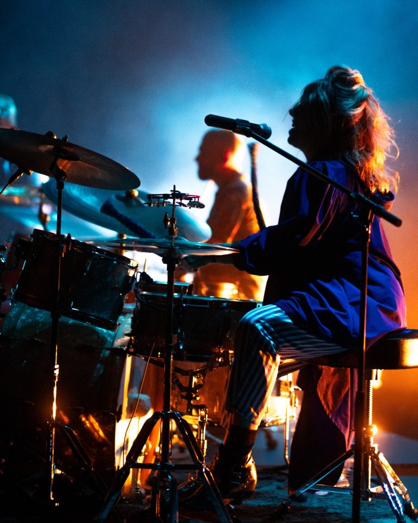 Sangue Suor no Quartel das Artes 2025 – baterista a tocar com luz azul e laranja – fotografia de concertos xpectrum