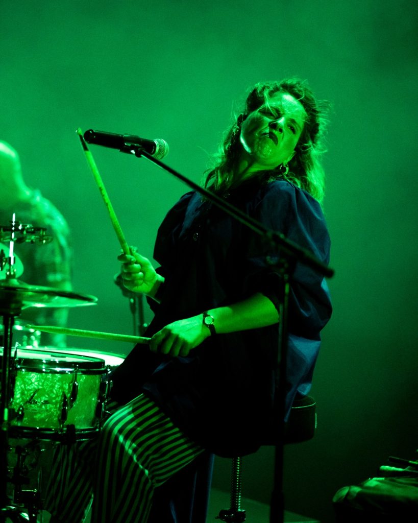 Sangue Suor no Quartel das Artes 2025 – baterista com luz verde intensa segurando baquetas – fotografia de concertos xpectrum