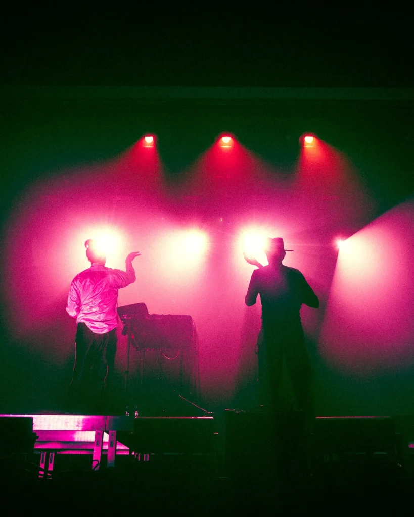 Plano geral do palco do Quartel das Artes com António Bastos e músico em contraluz vermelho durante concerto em 2026
