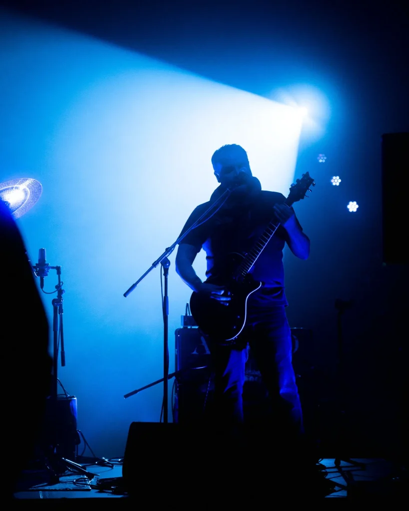 Guitarrista dos Avesso em silhueta sob feixe de luz azul no palco do Quartel das Artes em 2025, fotografia de concertos por xpectrum.