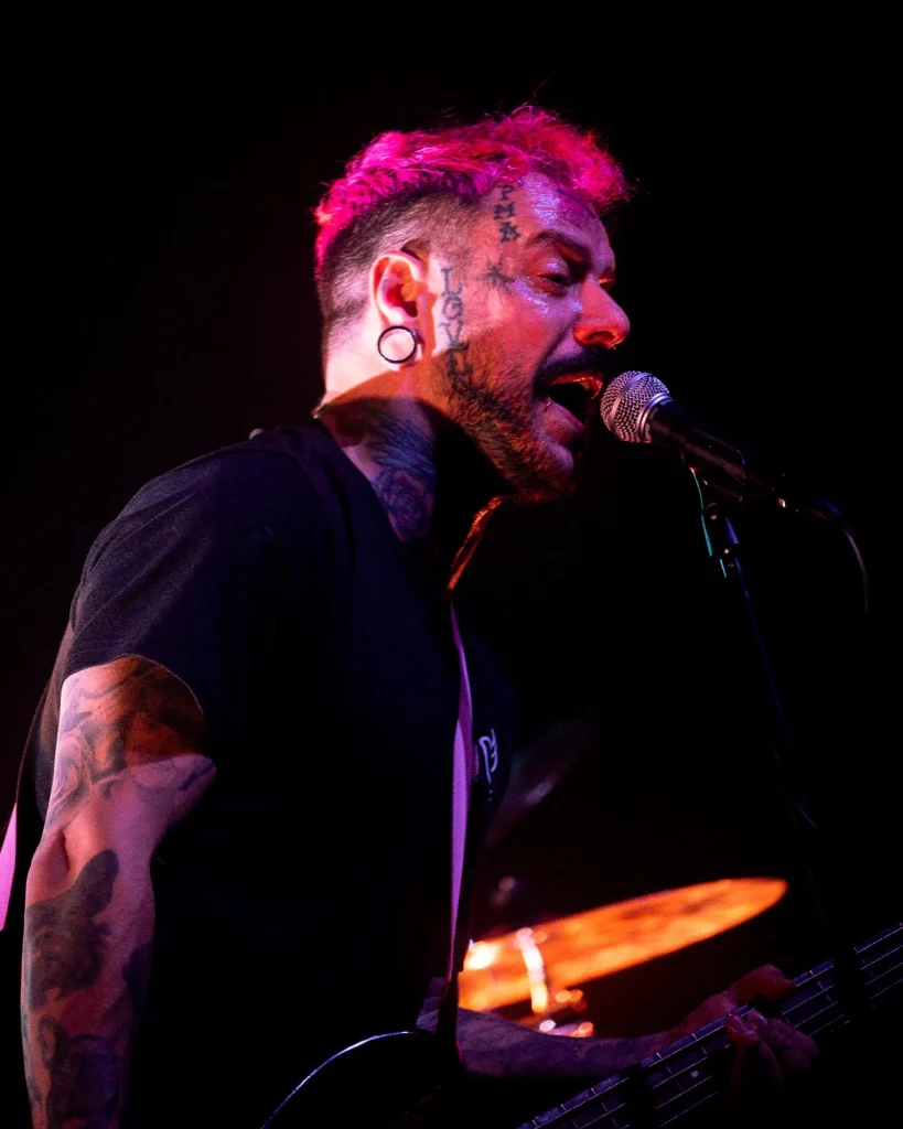 Baixista e vocalista dos Avesso de cabelo cor-de-rosa e tatuagens no rosto a cantar ao microfone em close-up no Quartel das Artes em 2025, fotografia de concertos xpectrum.