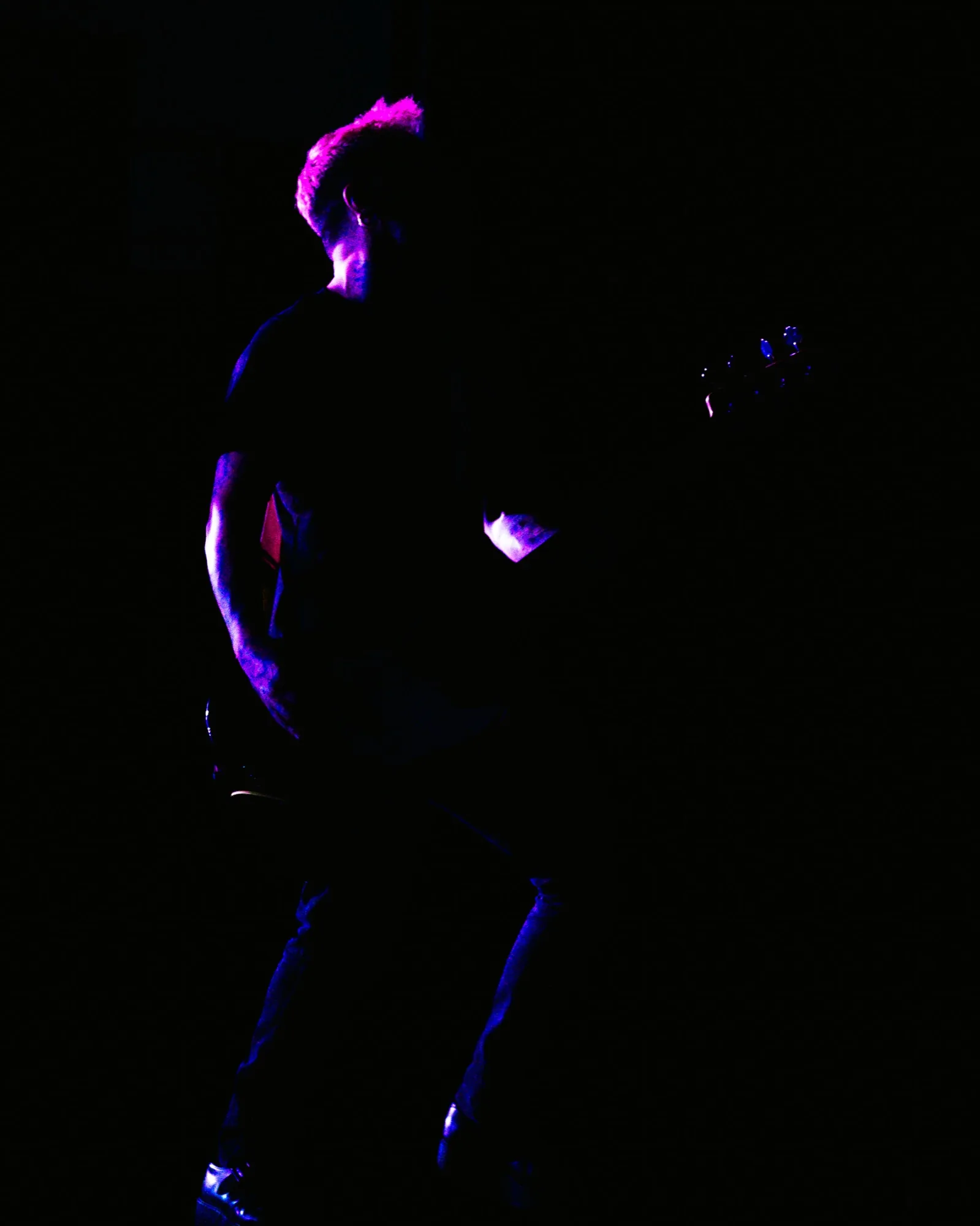 Baixista dos Avesso recortado em silhueta com cabelo iluminado a magenta no escuro do palco do Quartel das Artes em 2025, fotografia de concertos xpectrum.