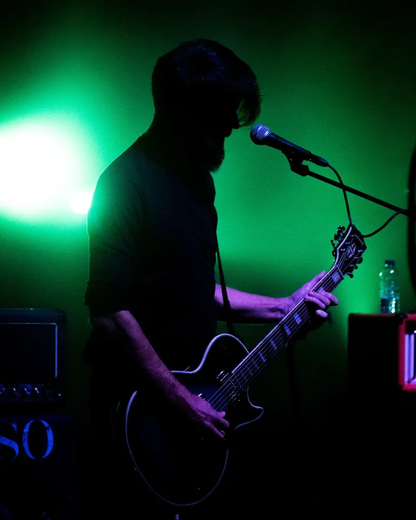 Guitarrista dos Avesso a tocar guitarra elétrica junto ao microfone com fundo iluminado a verde no Quartel das Artes em 2025, fotografia de concertos xpectrum.
