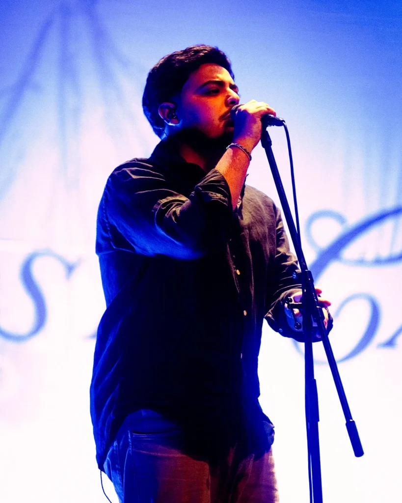 Vocalista dos Bandidos do Cante a cantar ao microfone sob luz azul, em concerto no Quartel das Artes em 2025, fotografia de concertos por xpectrum.