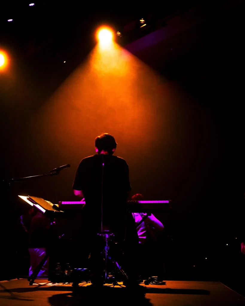 Tecladista dos Bandidos do Cante de costas ao palco sob feixe de luz laranja sobre fumo no Quartel das Artes em 2025, fotografia de concertos por xpectrum.