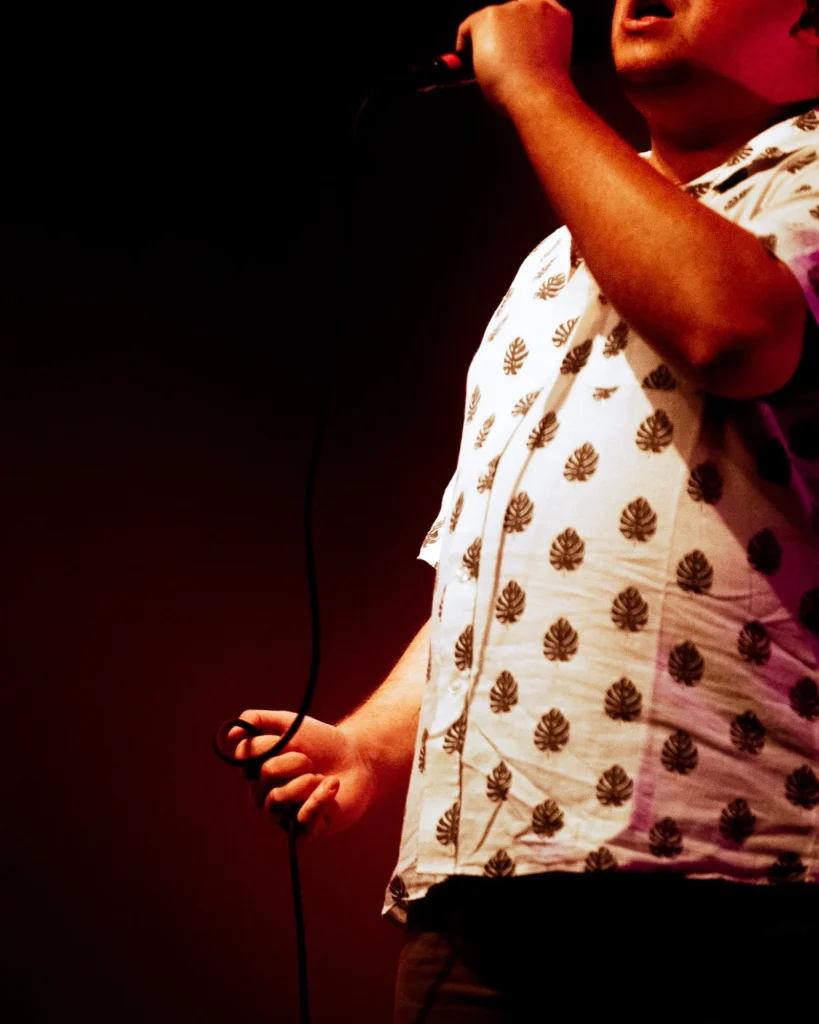 Pormenor do vocalista dos Bandidos do Cante a segurar microfone, com camisa estampada de folhas, no Quartel das Artes em 2025, fotografia de concertos por xpectrum.