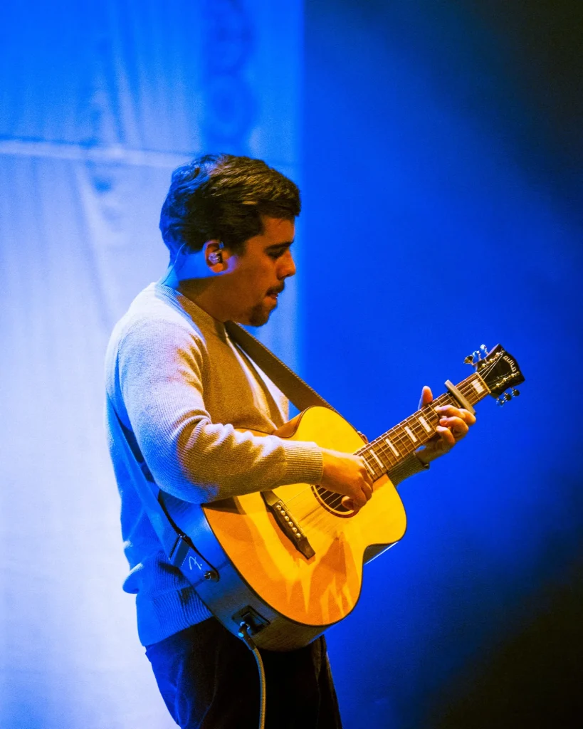 Guitarrista dos Bandidos do Cante a tocar guitarra acústica banhado por luz azul e laranja no Quartel das Artes em 2025, fotografia de concertos xpectrum.