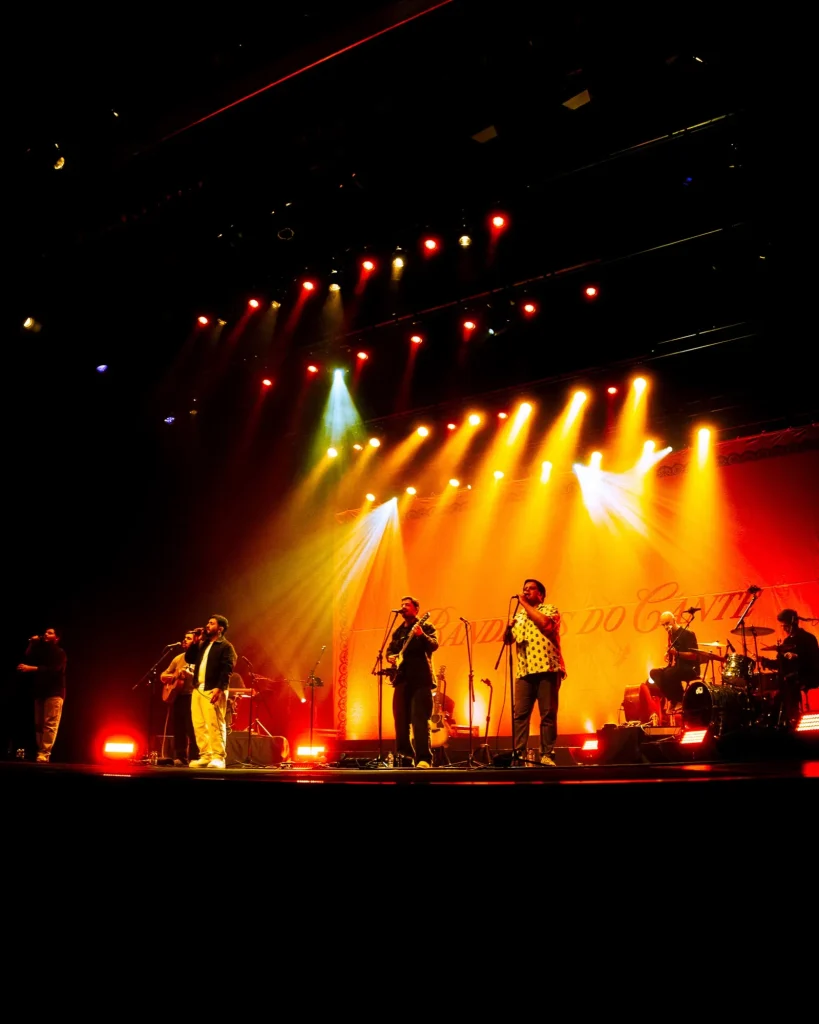 Plano geral do palco do Quartel das Artes em 2025 com os Bandidos do Cante em concerto sob feixes de luz vermelhos e laranjas, fotografia de concertos xpectrum.