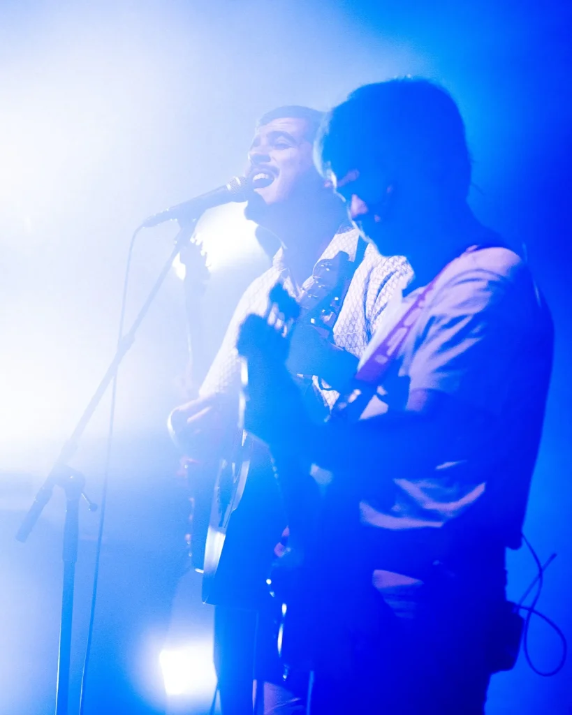 Dois elementos dos Duque Província a cantar ao microfone envolvidos em fumo e contraluz azul intenso no Quartel das Artes em 2025, fotografia de concertos xpectrum.