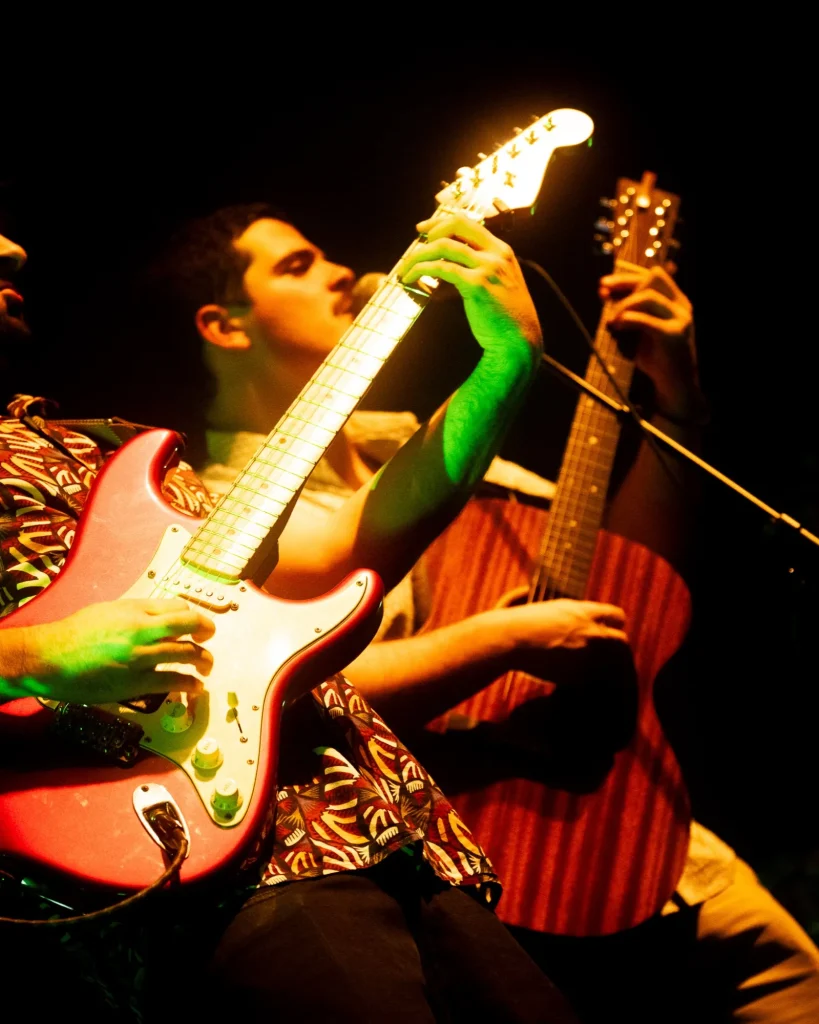 Guitarrista dos Duque Província de camisa estampada a tocar sob luz quente no Quartel das Artes em 2025, fotografia de concertos xpectrum.