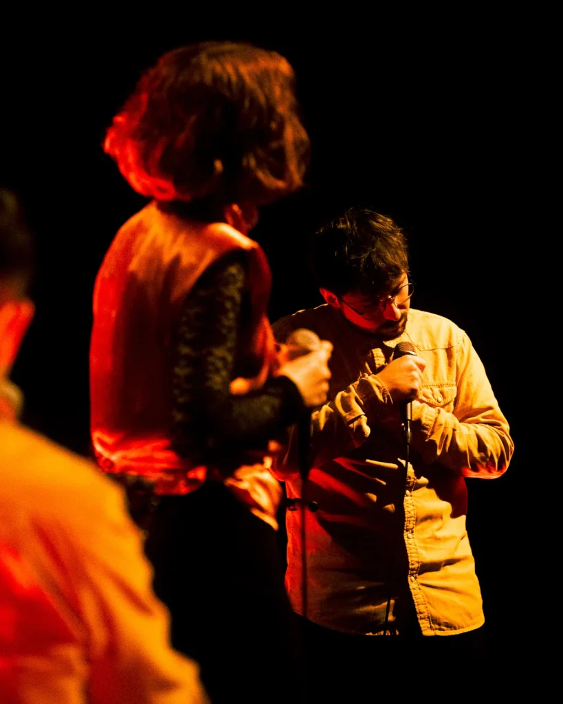 Vocalista dos Equinócio com convidado ao microfone sob luz quente vermelha no concerto do Quartel das Artes 2025
