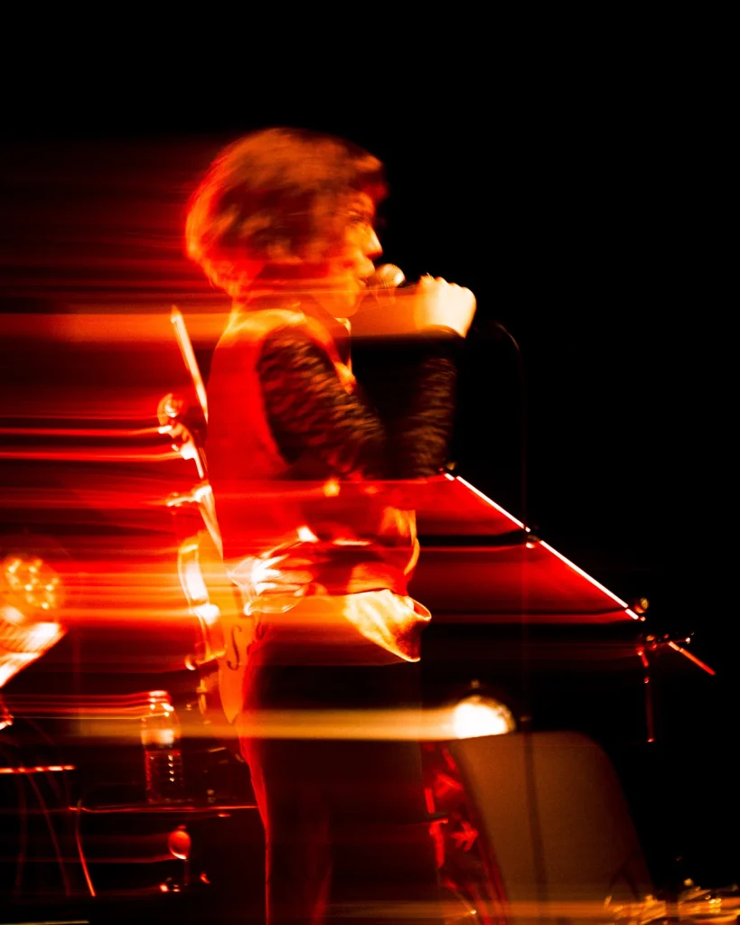 Vocalista dos Equinócio a cantar com efeito de movimento e rastos de luz vermelha no Quartel das Artes 2025