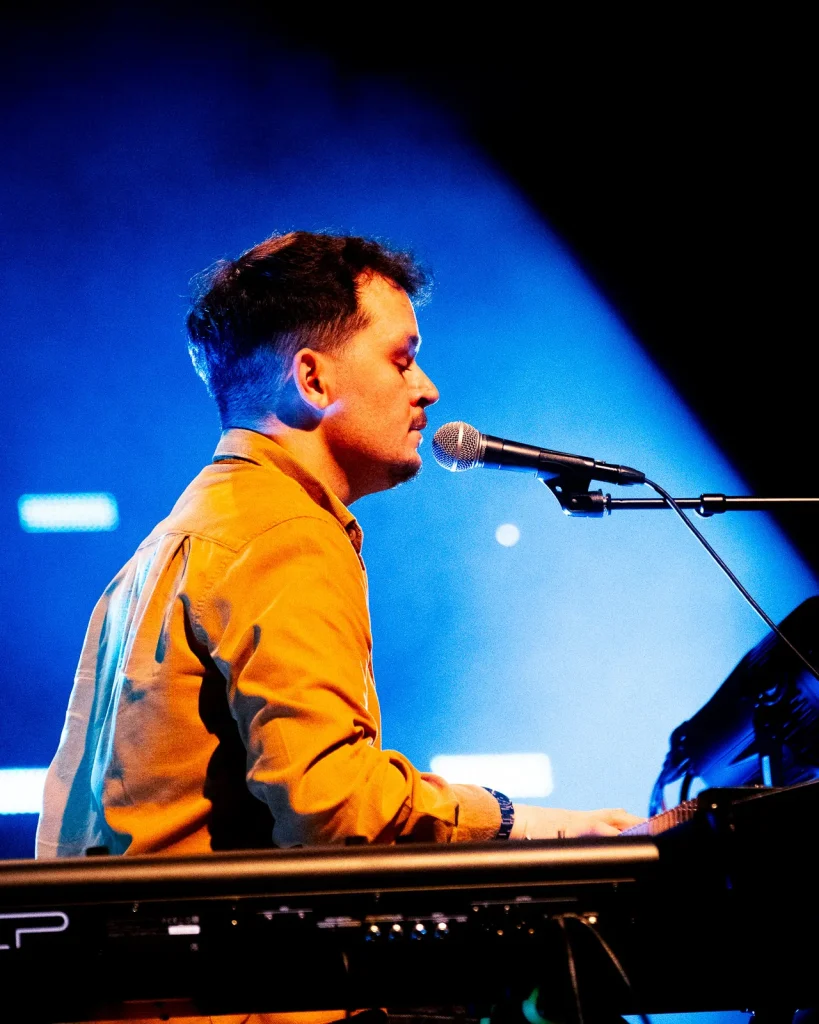 Diogo dos Equinócio a cantar e tocar teclado sob luz azul de palco no concerto do Quartel das Artes 2025