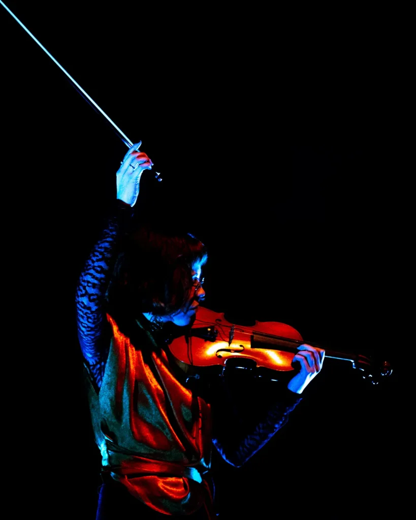 Violinista dos Equinócio a tocar com arco erguido sob luz azul intensa no concerto do Quartel das Artes 2025