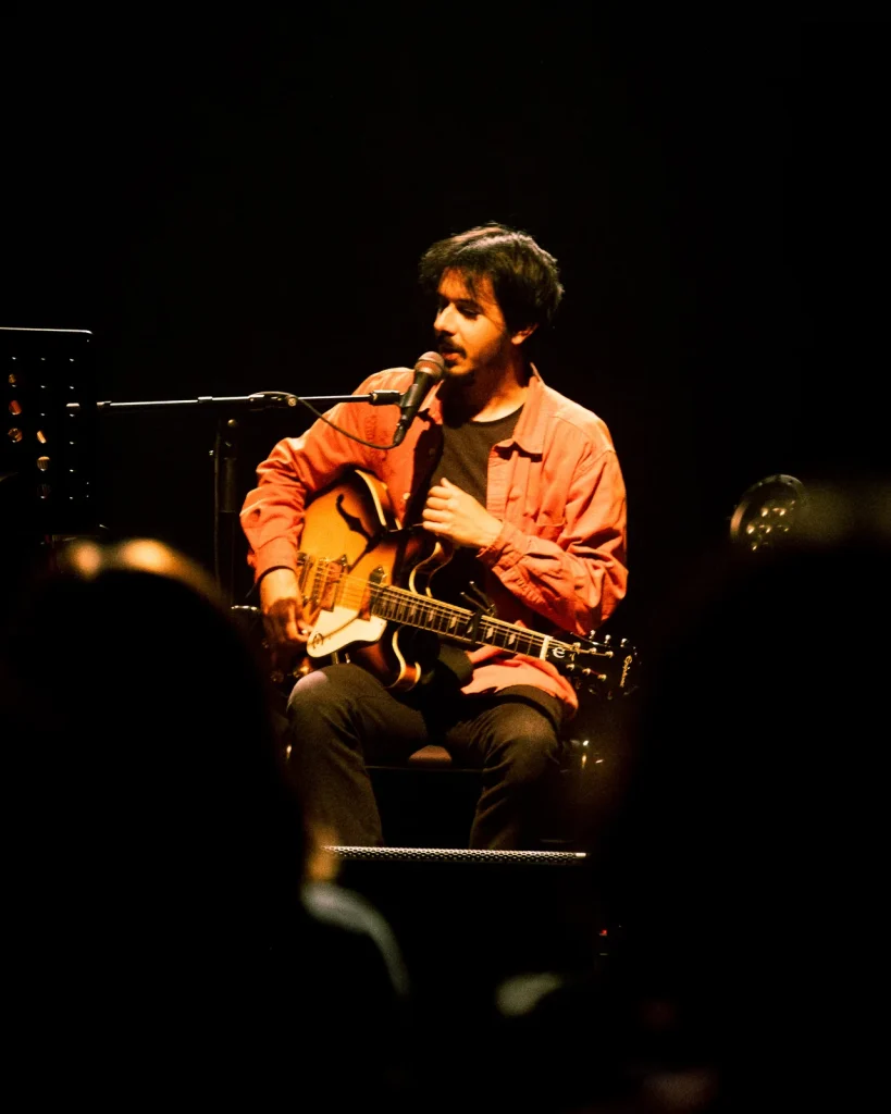 Convidado dos Equinócio sentado a cantar e tocar guitarra semi-acústica em frente ao público no Quartel das Artes 2025