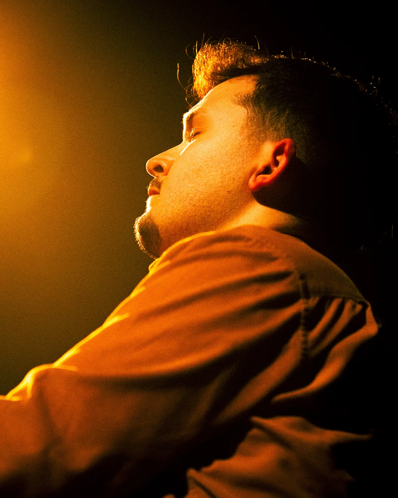 Retrato de perfil de músico dos Equinócio com olhos fechados sob luz quente lateral no concerto do Quartel das Artes 2025