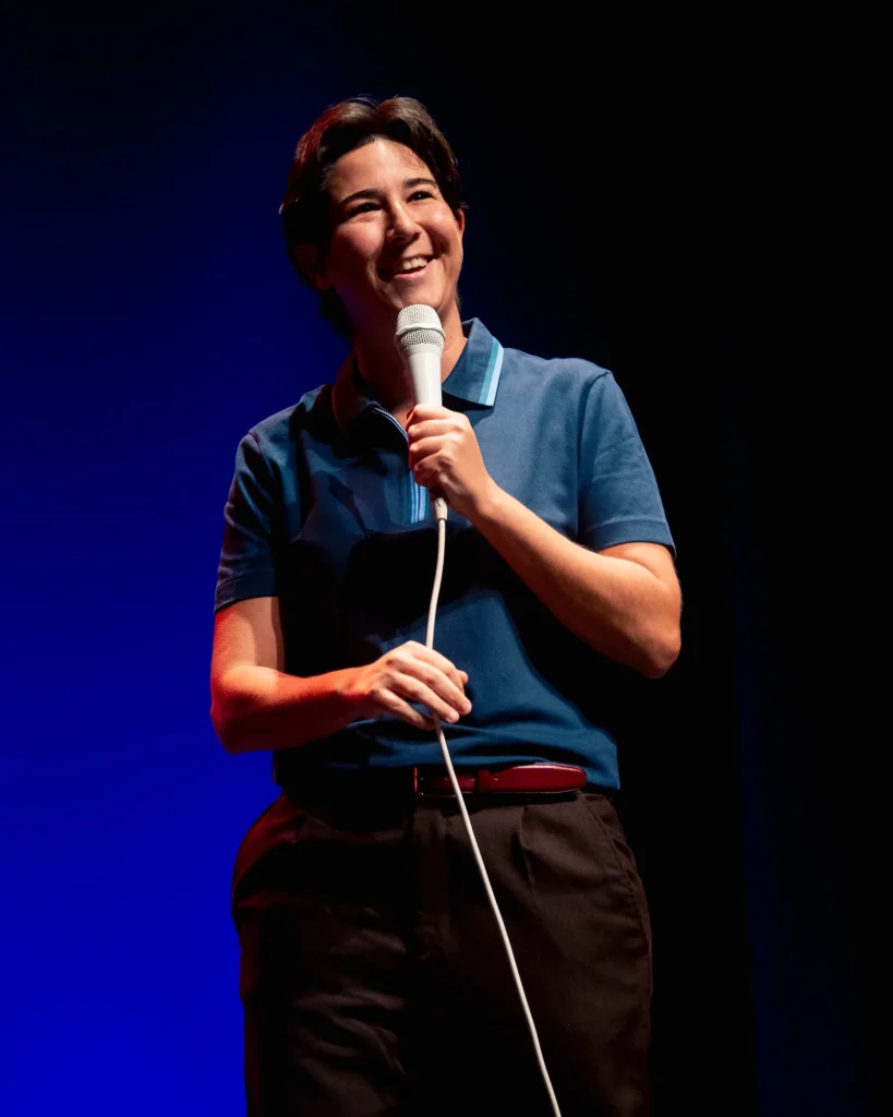 Plano aproximado de Luana do Bem a sorrir abertamente com o microfone junto ao peito durante o stand-up no Quartel das Artes em 2025 — fotografia de espetáculo de humor por xpectrum.