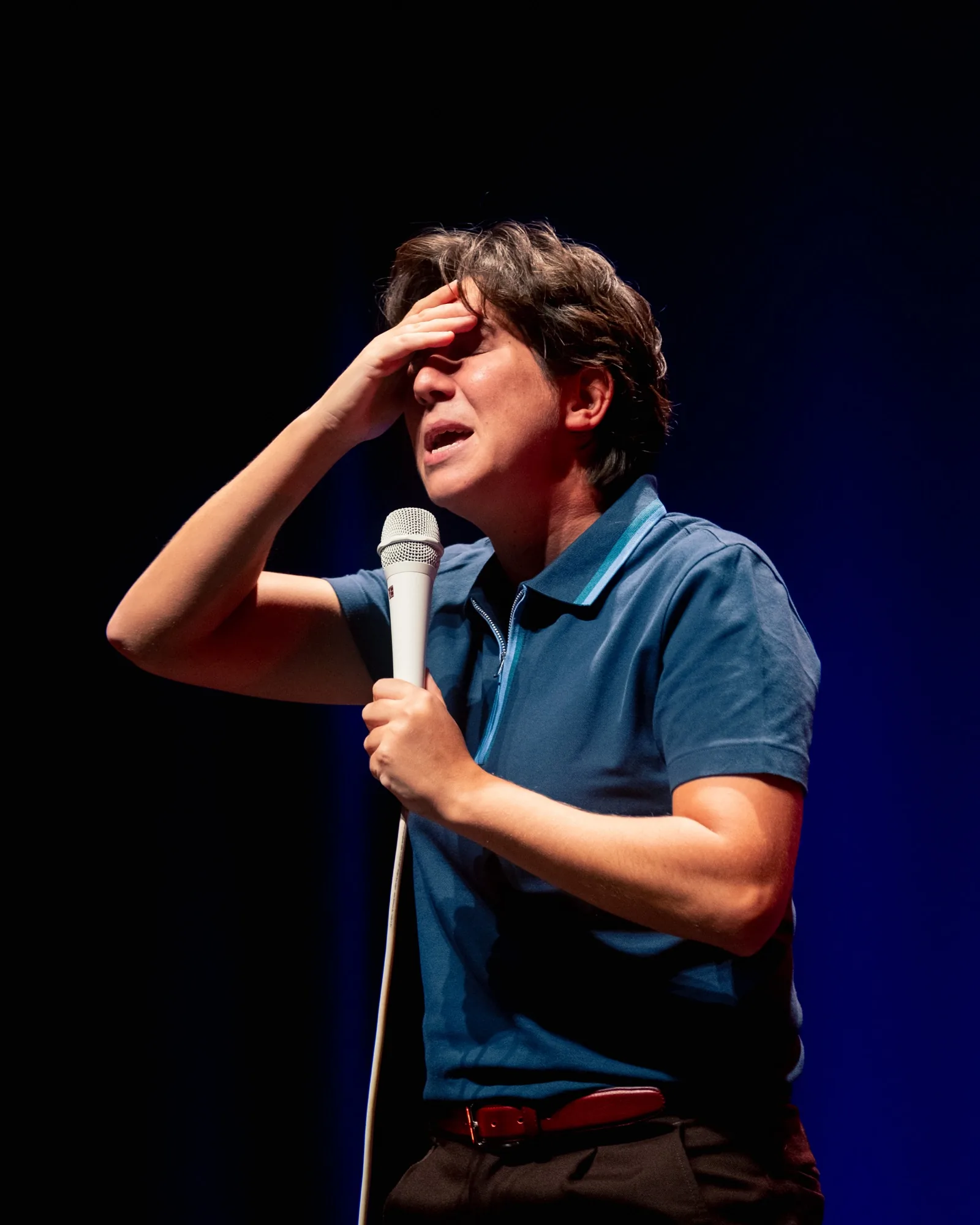Luana do Bem com a mão na testa em expressão cómica de desespero, microfone junto ao peito durante o stand-up no Quartel das Artes em 2025 — fotografia de espetáculo de humor por xpectrum.