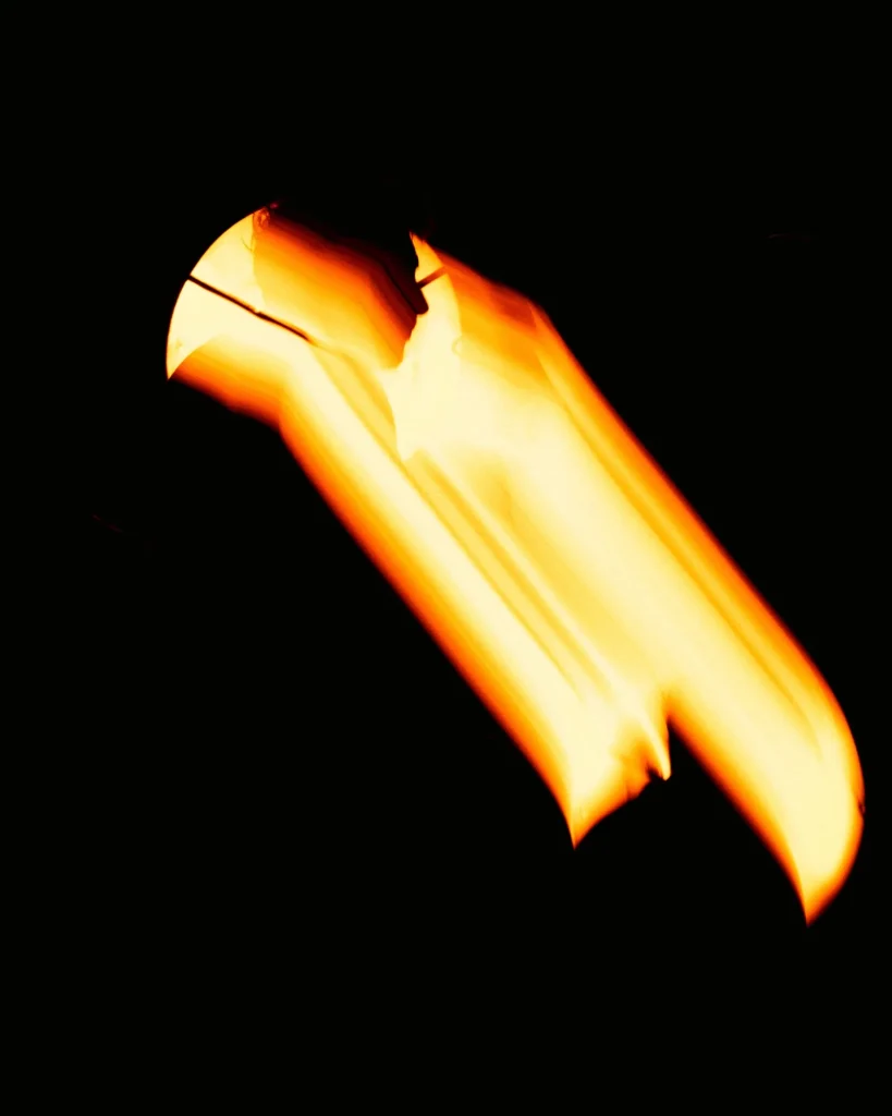 Pormenor cénico abstrato com a luz quente do candeeiro de palco a desenhar formas alaranjadas sobre fundo preto durante o concerto de Rui Massena no Quartel das Artes em 2025, fotografia de concertos por xpectrum.
