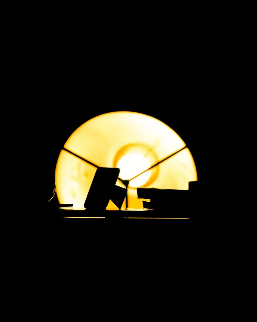 Pormenor cénico do candeeiro de palco com luz amarela em contraluz a recortar a silhueta de objetos sobre o piano no concerto de Rui Massena no Quartel das Artes em 2025, fotografia de concertos por xpectrum.