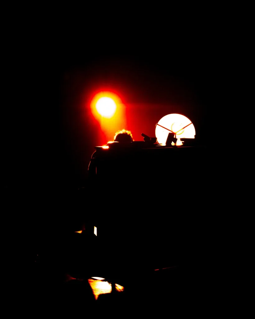 Plano largo de Rui Massena ao piano em silhueta, com um foco vermelho intenso e o candeeiro amarelo a marcarem a cenografia do concerto no Quartel das Artes em 2025, fotografia de concertos por xpectrum.