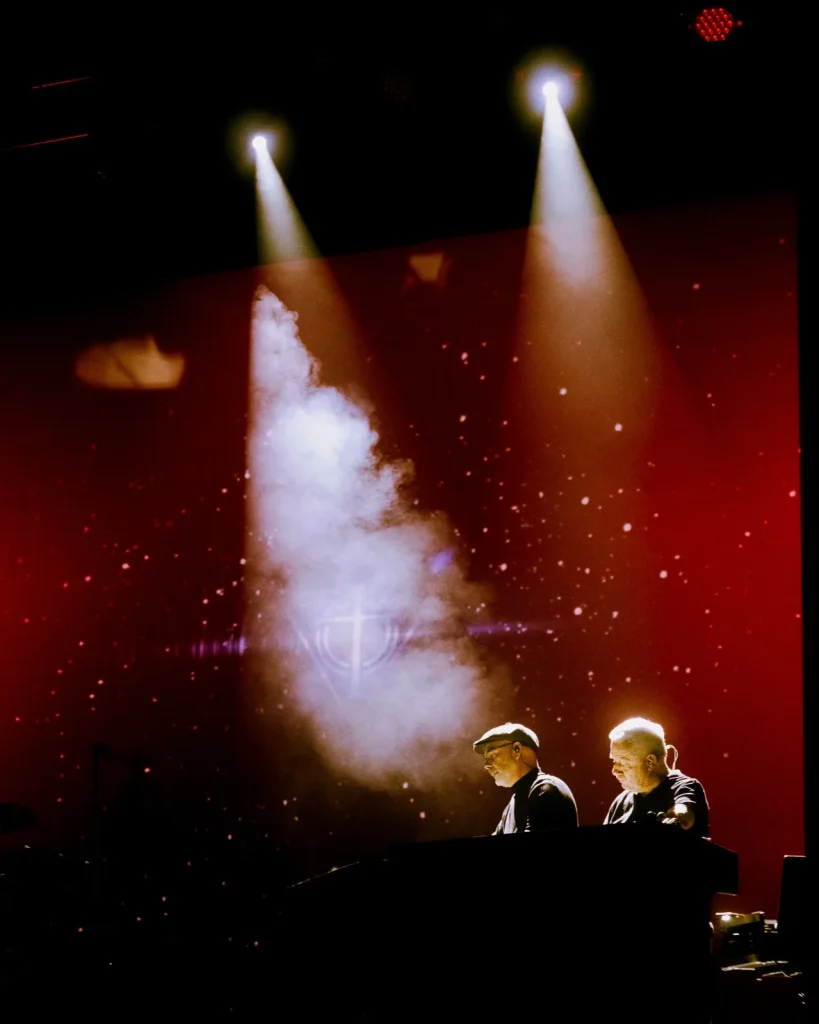 Tributus em concerto no Quartel das Artes 2025: dupla aos teclados sob feixes brancos e visual do prisma de Pink Floyd