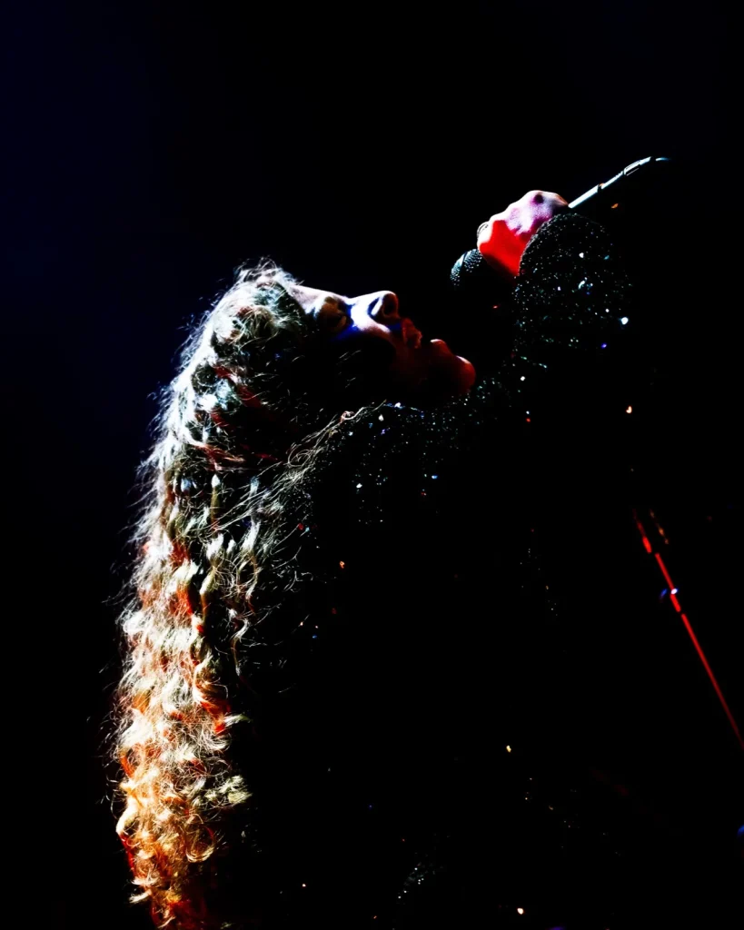 Vocalista dos Tributus a cantar com cabelo encaracolado iluminado — concerto tributo a Pink Floyd no Quartel das Artes