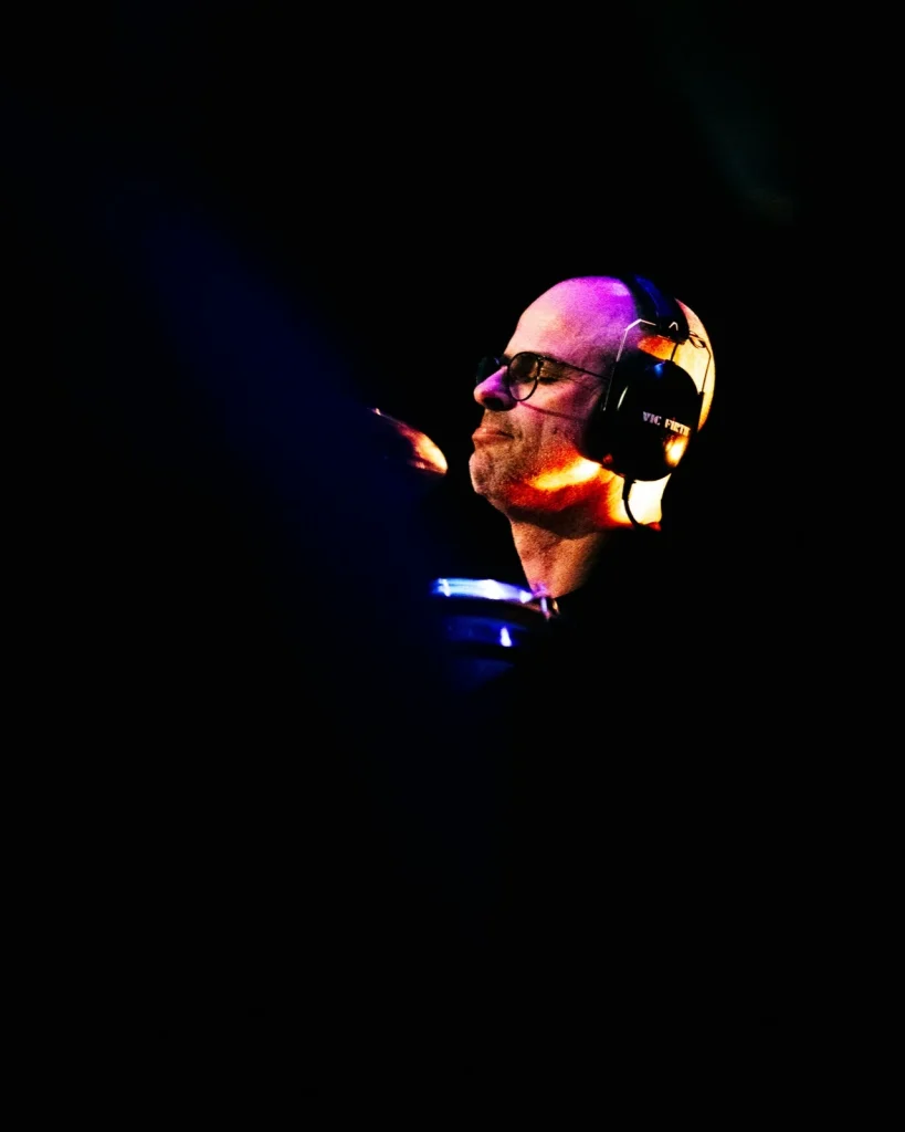 Baterista dos Tributus de auscultadores, perfil iluminado em luz roxa e âmbar — concerto Pink Floyd no Quartel das Artes