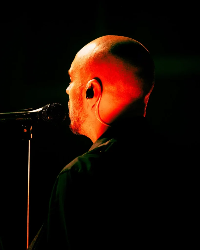 Perfil do vocalista dos Tributus a cantar sob luz vermelha intensa — tributo a Pink Floyd no Quartel das Artes, 2025